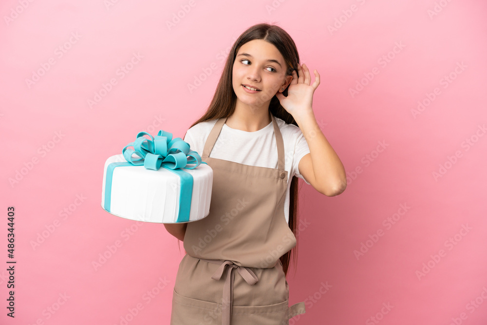 Little girl with a big cake over isolated pink background listening to something by putting hand on the ear Little girl with a big cake over isolated pink background listening to something by putting hand on the ear