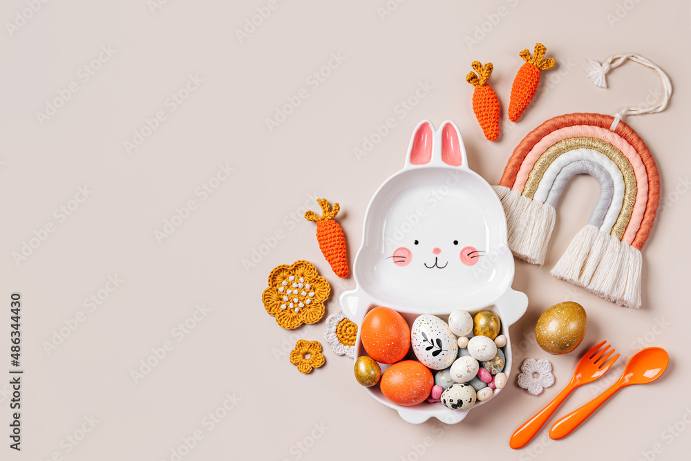 Obraz premium Easter decoration with cute plate in the shape of a bunny with Easter eggs, candy, carrot and flowers. Happy Easter concept. Idea for Easter dinner