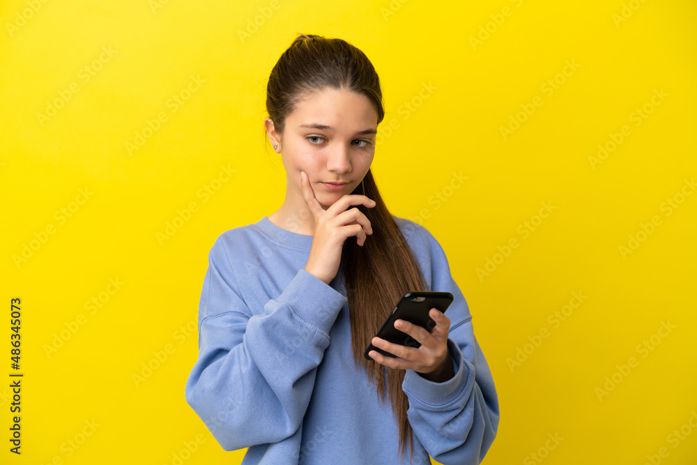 Little girl over isolated yellow background using mobile phone and thinking Little girl over isolated yellow background using mobile phone and thinking