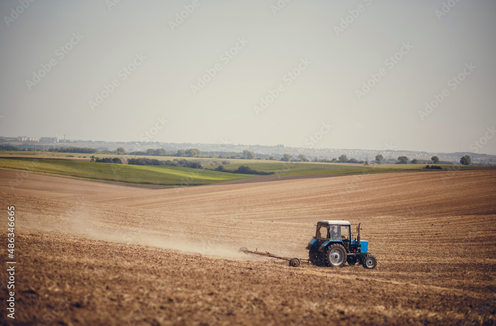 Fototapeta premium Agriculture use tractor plowing land field. Cultivated field. Agronomy, farming, husbandry .Tractor working on farm,modern agricultural transport,farmer working in the field