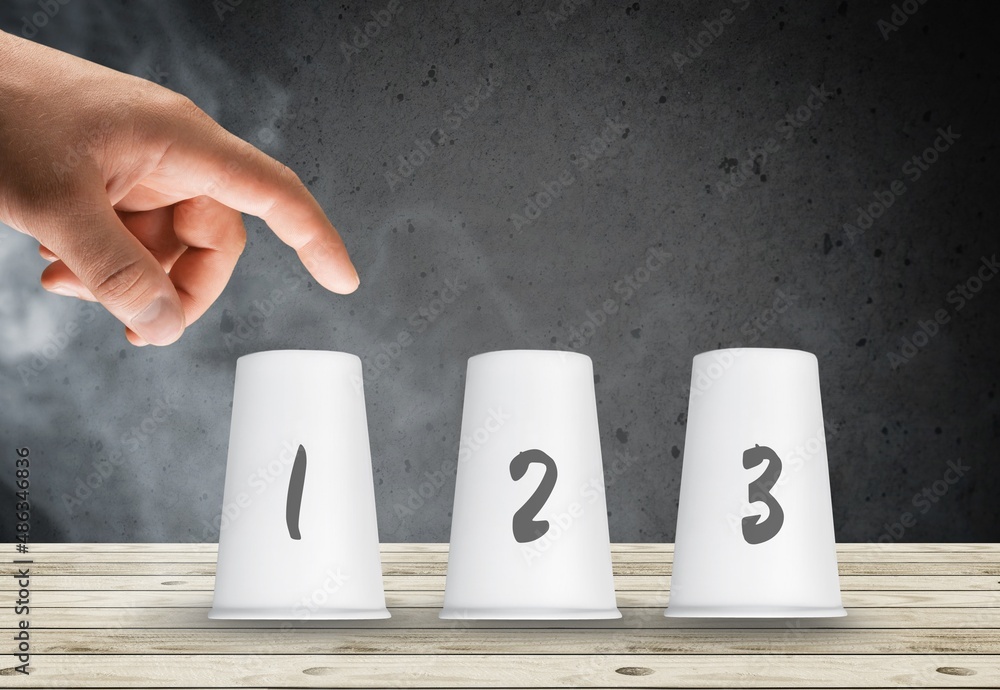 Person's hand play the guessing shell game with paper cups on the table ...