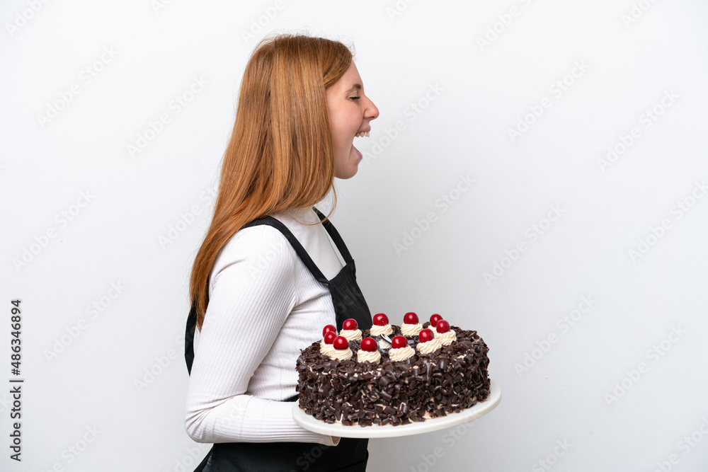 Young redhead woman holding birthday cake isolated on white background laughing in lateral position