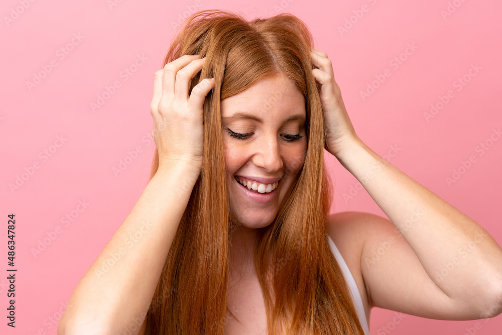Young redhead woman isolated on pink background touching her hair. Close up portrait
