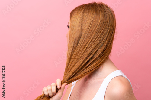 Young redhead woman isolated on pink background touching her hair. Close up portrait
