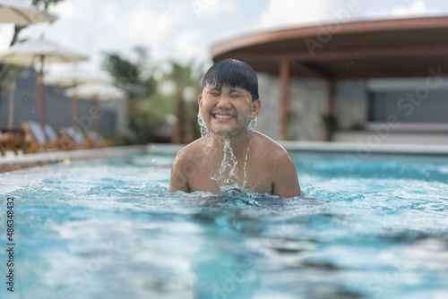Asian Young Boy Having a good time in swimming pool  He Jumping and Playing a Water in Summer.
