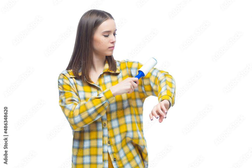 Portrait of young woman using a lint remover to clean yellow checkered shirt from dust, hair, lint and fluff, isolated on white background Portrait of young woman using a lint remover to clean yellow checkered shirt from dust, hair, lint and fluff, isolated on white background