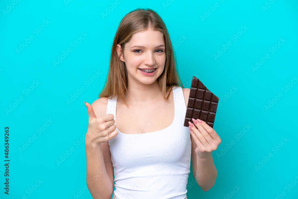 Teenager Russian girl isolated on blue background taking a chocolate tablet and with thumb up Teenager Russian girl isolated on blue background taking a chocolate tablet and with thumb up