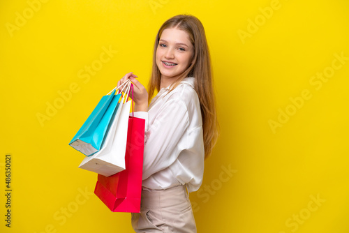 Teenager Russian girl isolated on yellow background holding shopping bags and smiling