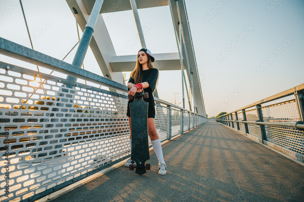 Young woman holding her longboard and standing on the bridge