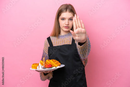 Teenager Russian girl holding a waffles isolated on pink background making stop gesture