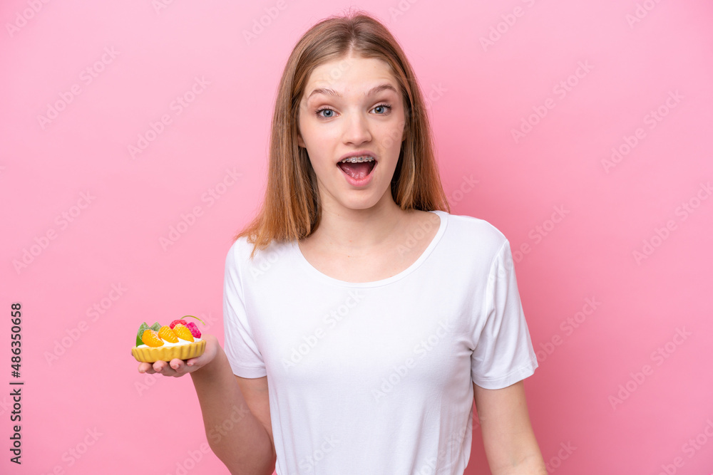 Teenager Russian girl holding a tartlet isolated on pink background with surprise facial expression Teenager Russian girl holding a tartlet isolated on pink background with surprise facial expression