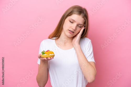 Teenager Russian girl holding a tartlet isolated on pink background with headache