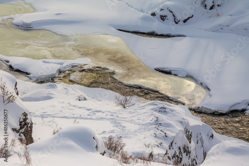 Winter landscape with a fast river with ice-free water  snow and a stone bank