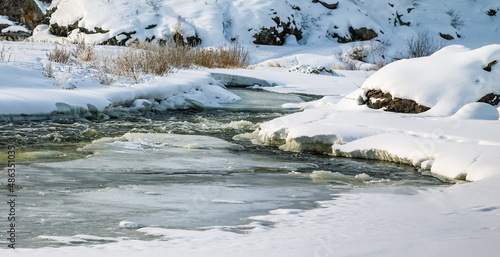 Winter landscape with a fast river with ice-free water  snow  dry grass and rocky shores