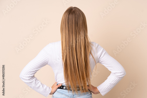 Teenager Ukrainian girl isolated on beige background in back position