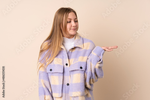 Teenager Ukrainian girl isolated on beige background holding copyspace with doubts