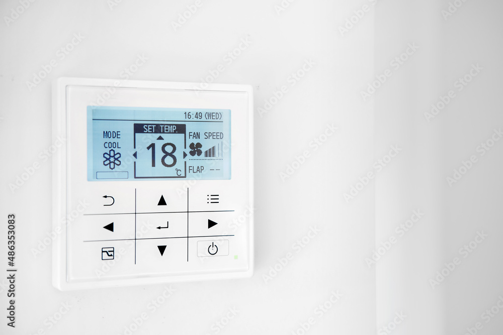 Mounted on wall, climate control show 18 degrees indoor, remote air-conditioner inside smart home close up view, no people. Modern tech, comfort living concept Mounted on wall, climate control show 18 degrees indoor, remote air-conditioner inside smart home close up view, no people. Modern tech, comfort living concept