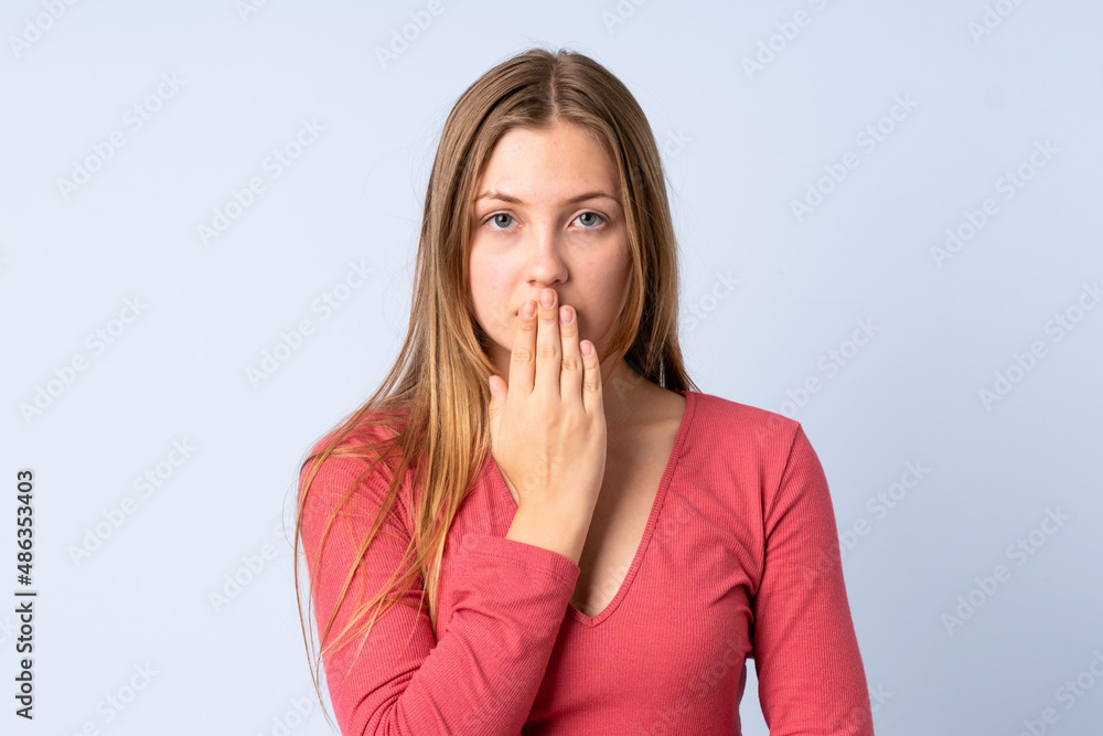 Teenager Ukrainian girl isolated on blue background covering mouth with hand Teenager Ukrainian girl isolated on blue background covering mouth with hand