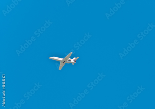 bottom view, very far distance of a private, twin, passenger jet, with a blue sky background
