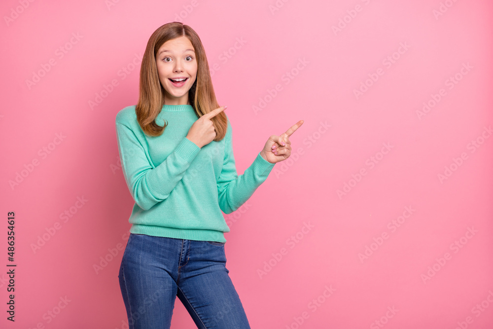Photo of excited funky school girl dressed teal pullover pointing empty space isolated pink color background Photo of excited funky school girl dressed teal pullover pointing empty space isolated pink color background
