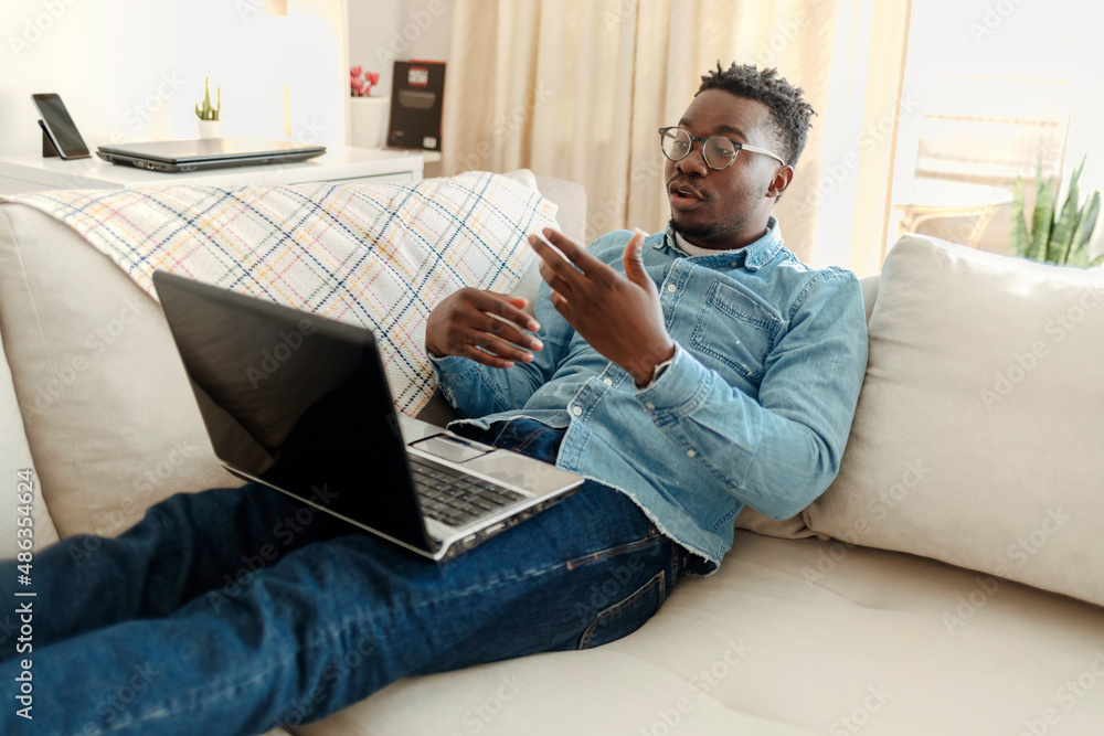 Shot of a young happy man using a laptop on the sofa at home. Shot of a handsome young man using a laptop at home while sitting on gray sofa during the day. Shot of a young happy man using a laptop on the sofa at home. Shot of a handsome young man using a laptop at home while sitting on gray sofa during the day.