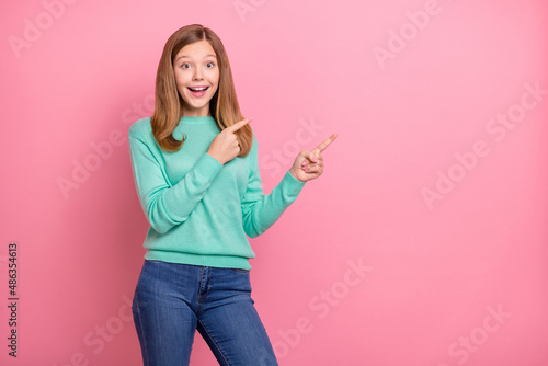 Photo of excited funky school girl dressed teal pullover pointing empty space isolated pink color background © deagreez