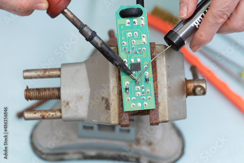 Manos con soldador y estaño, soldando una soldadura defectuosa de un circuito electrónico photo