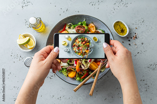 Woman taking photo of vegetable salad with smartphone. Posting food pictures (images) on social media.