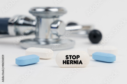 On a white surface lie pills, a stethoscope and a tablet with the inscription - STOP HERNIA