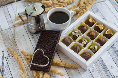 Handmade candies and coffee in a porcelain cup and heart with a rope on a chocolate bar on a gray wooden background.