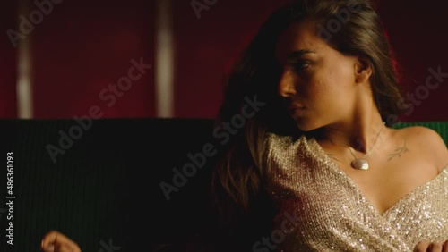 4K Beautiful attractive woman sitting on sofa and dancing, flirting, posing, looking into camera with shiny dress . Fashion advertisement concept . Shot on ARRI cinema camera in slow motion