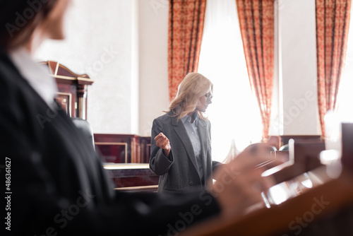Obraz na płótnie middle aged advocate pointing with hand at blurred witness during questioning in