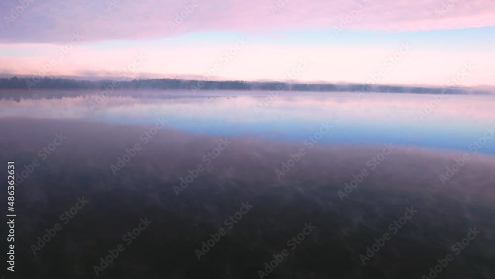 Foggy morning at the lake, mirror image. Slow drone flight low over the blue water during sunrise, zoom out. Foggy morning at the lake, mirror image. Slow drone flight low over the blue water during sunrise, zoom out.