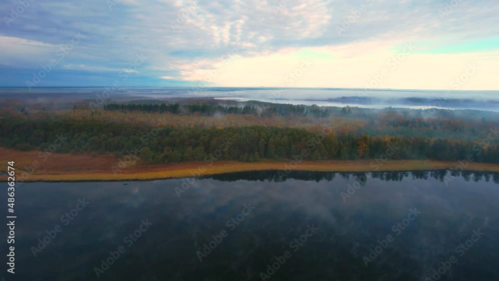 Aerial view of the foggy morning at the lake surrounded by the forest, autumn colors. Blue sky and white clouds. Slow drone flight over the water, zoom out. Aerial view of the foggy morning at the lake surrounded by the forest, autumn colors. Blue sky and white clouds. Slow drone flight over the water, zoom out.