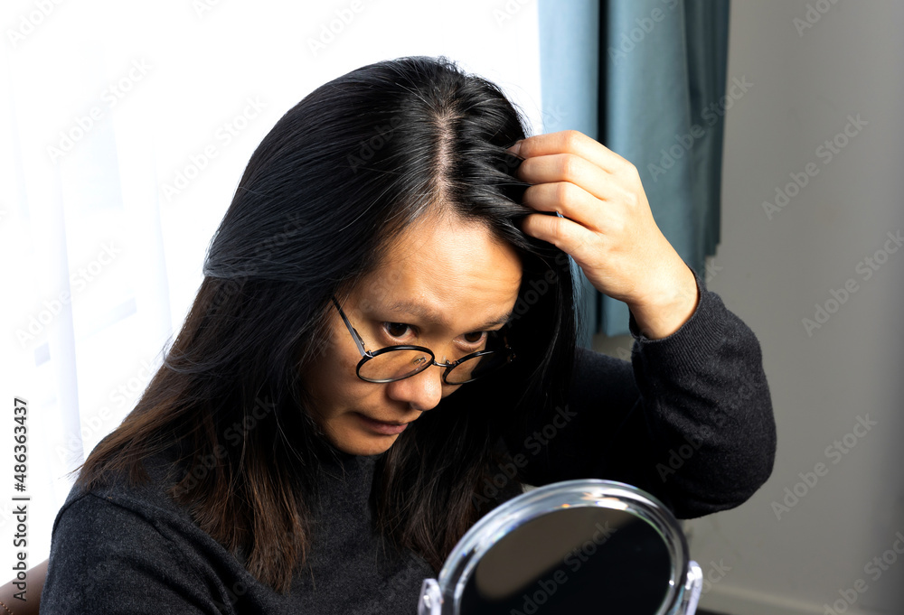 Young asian woman checking in the mirror to looking at the hairs turn gray  too early. Young woman be worrying because of hair root turn white from  stress. Stock Photo | Adobe