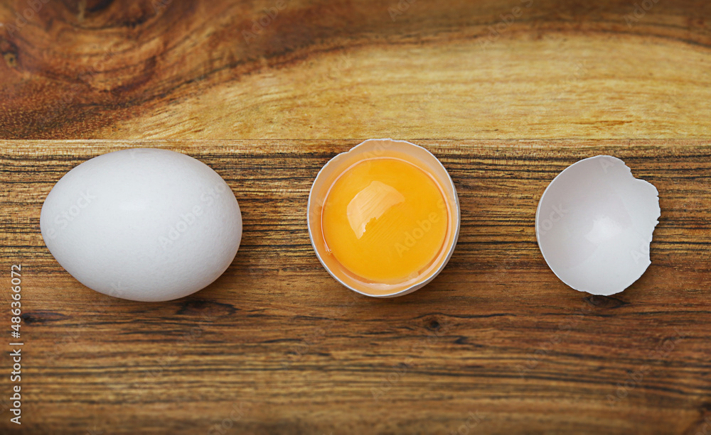 Fresh white chicken eggs and egg half with a yolk on wooden table. Top view. Fresh white chicken eggs and egg half with a yolk on wooden table. Top view.