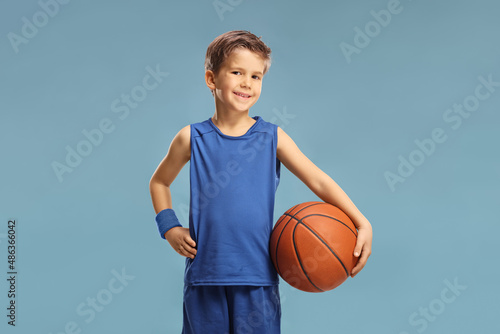 Boy in a blue jersey holding a basketball isolated on blue © Ljupco Smokovski