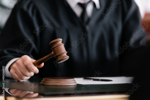 Fototapet partial view of blurred judge in robe holding gavel in court