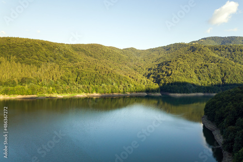 Aerial view of big lake with clear blue water between high mountain hills covered with dense evergreen forest