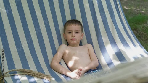 Small boy enjoying summertime outdoors. Child lying in a hammock on camping. Happiness, childhood, freedom concept.