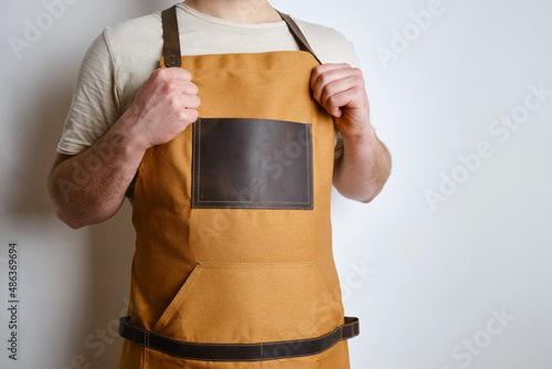 A man in a kitchen apron. Chef work in the cuisine. Cook in uniform, protection apparel. Job in food service. Professional culinary. Camel fabric apron, casual stylish clothing. Handsome baker posing 