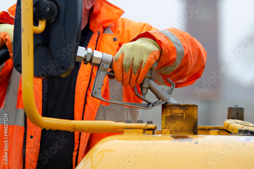 Construction worker in safety gloovs filling excavator with diesel fuel on construction site photo