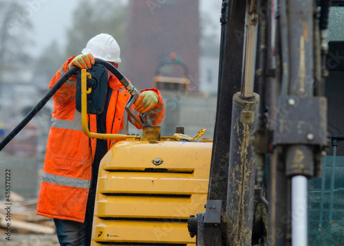 Construction worker in safety gloovs filling excavator with diesel fuel on building site