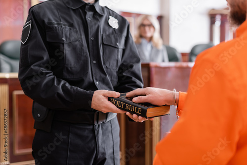 partial view of bailiff in uniform holding bible near accused man giving oath in court photo
