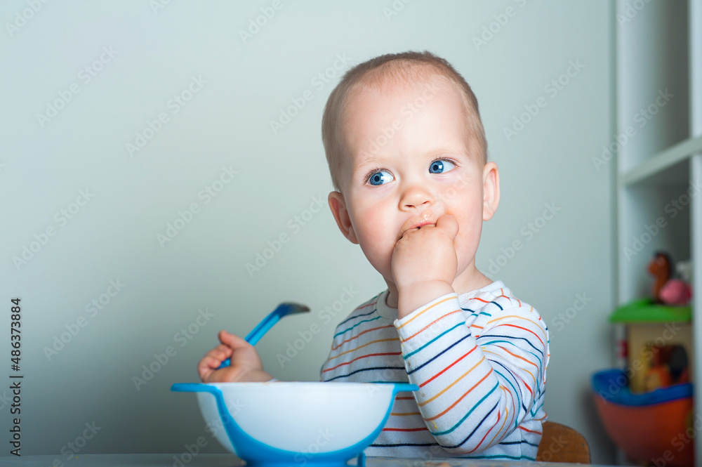 Toddler boy eats with spoon at table.. Toddler boy eats with spoon at table..