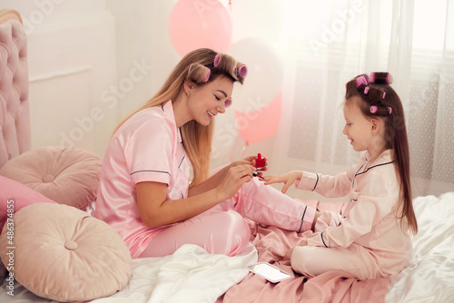 Happy loving family. Mother and daughter doing hair  manicure and having fun  sitting on the bed in the bedroom in pajamas.
