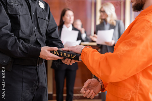 bailiff in uniform holding bible near accused man giving oath in court photo