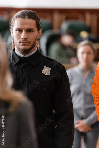 Obraz na plátně selective focus of bearded bailiff in black uniform near blurred jurors in court