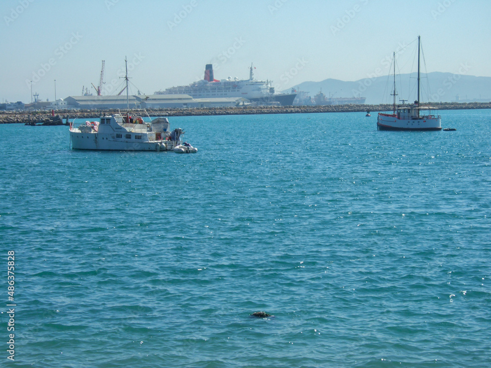 Some fishing boats and sailboats in front of the container port in algeciras spain. In the background you can see a steam ferry