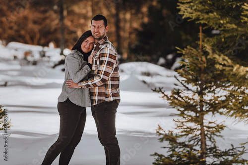 Beautiful couple hugging between snowy pines, woman in casual clothes holding hands on man chest. Selective focus photo